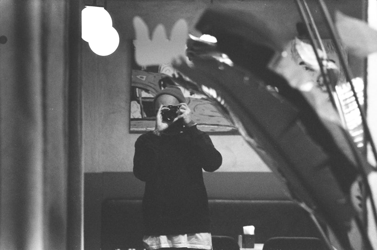 Monochrome image of a person taking a self-portrait with a camera in a mirror reflection.
